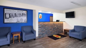 A reception area with a blue wall, two grey armchairs, a small wooden table, a stone wall, and a Super 8 logo on the floor.