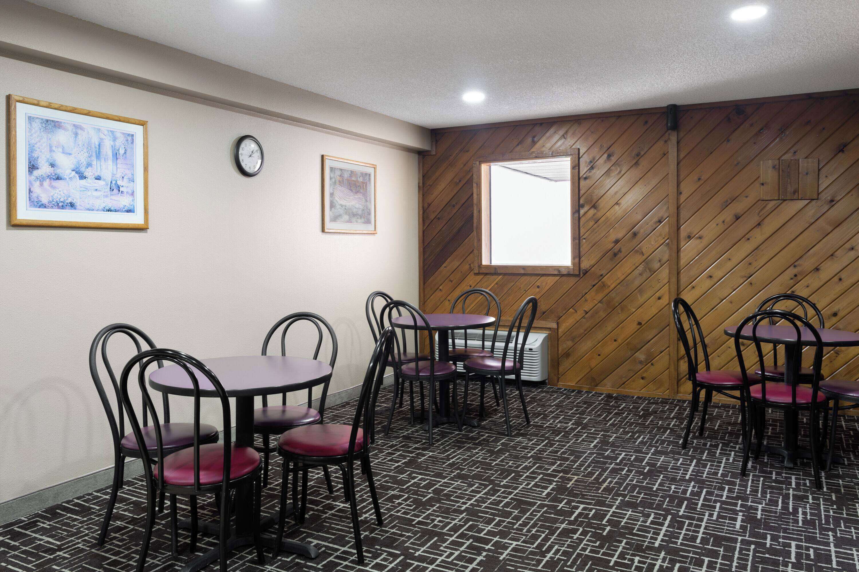 Une pièce comprenant quatre tables et des chaises, un lambris en bois, une horloge et des œuvres d’art encadrées accrochées aux murs.