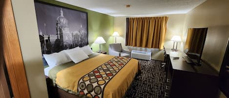 Una habitación de hotel con una cama, dos mesitas de noche con lámparas, un escritorio con silla, un ventanal con cortinas y un aire acondicionado de pared.
