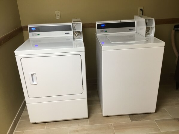 Two white front-loading washing machines with digital displays, placed side by side on a tiled floor. - Circle S Motel (Anamosa)