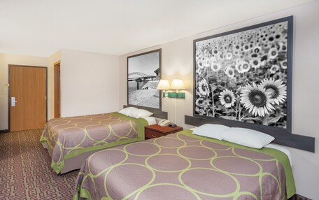 A hotel room with two beds, a large wall-mounted mirror, a nightstand with a lamp, and a framed picture of sunflowers.