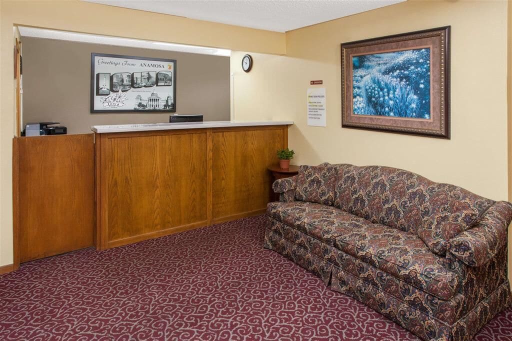 A reception area with a wooden desk, patterned carpet, a couch, a clock, and a framed picture on the wall.