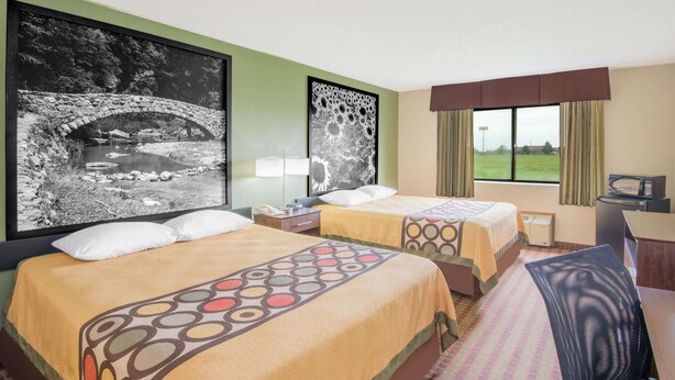 Une chambre d’hôtel avec deux lits, un bureau, une chaise, une télévision et une fenêtre donnant sur un paysage verdoyant.
