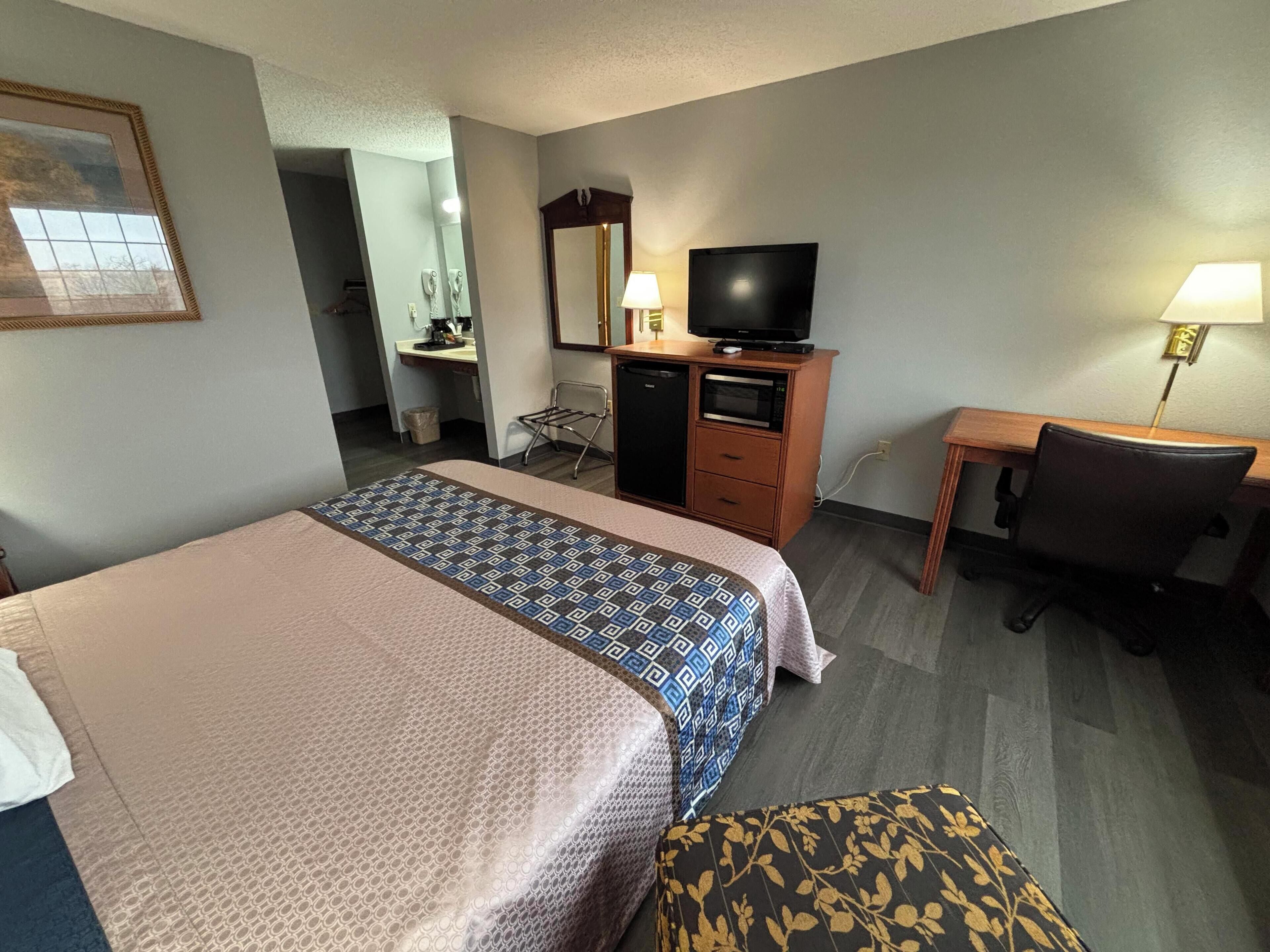 A hotel room with a bed, a desk, a television, and a chair.