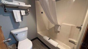 A bathroom with a toilet, a shower with a curtain, and a towel rack with towels. - Covered Bridge Inn (Winterset)