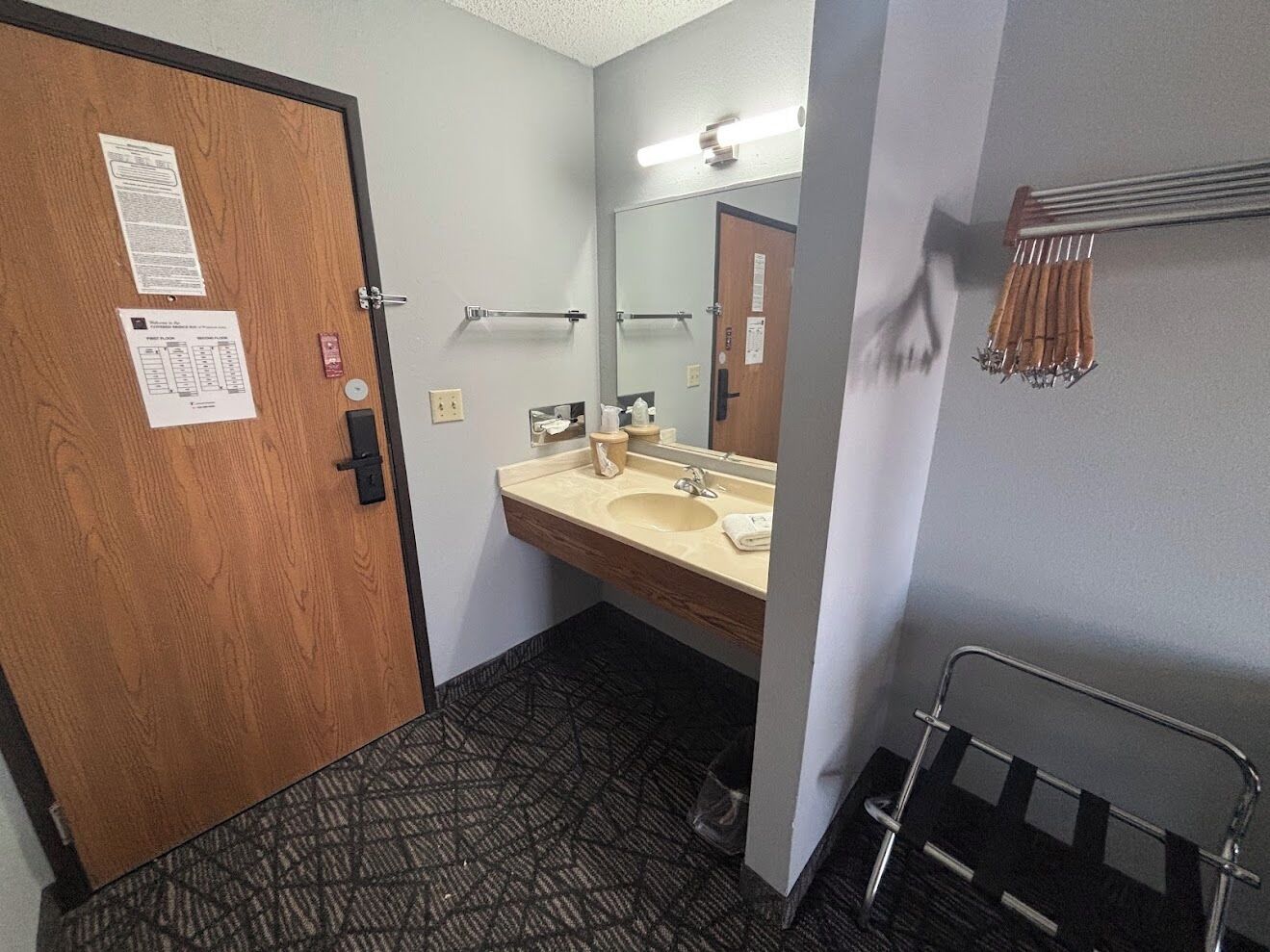 Un baño de hotel con puerta de madera, un lavabo con espejo, un perchero para toallas y un suelo estampado.