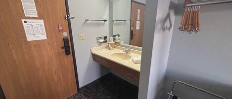 Un baño de hotel con puerta de madera, un lavabo con espejo, un perchero para toallas y un suelo estampado.