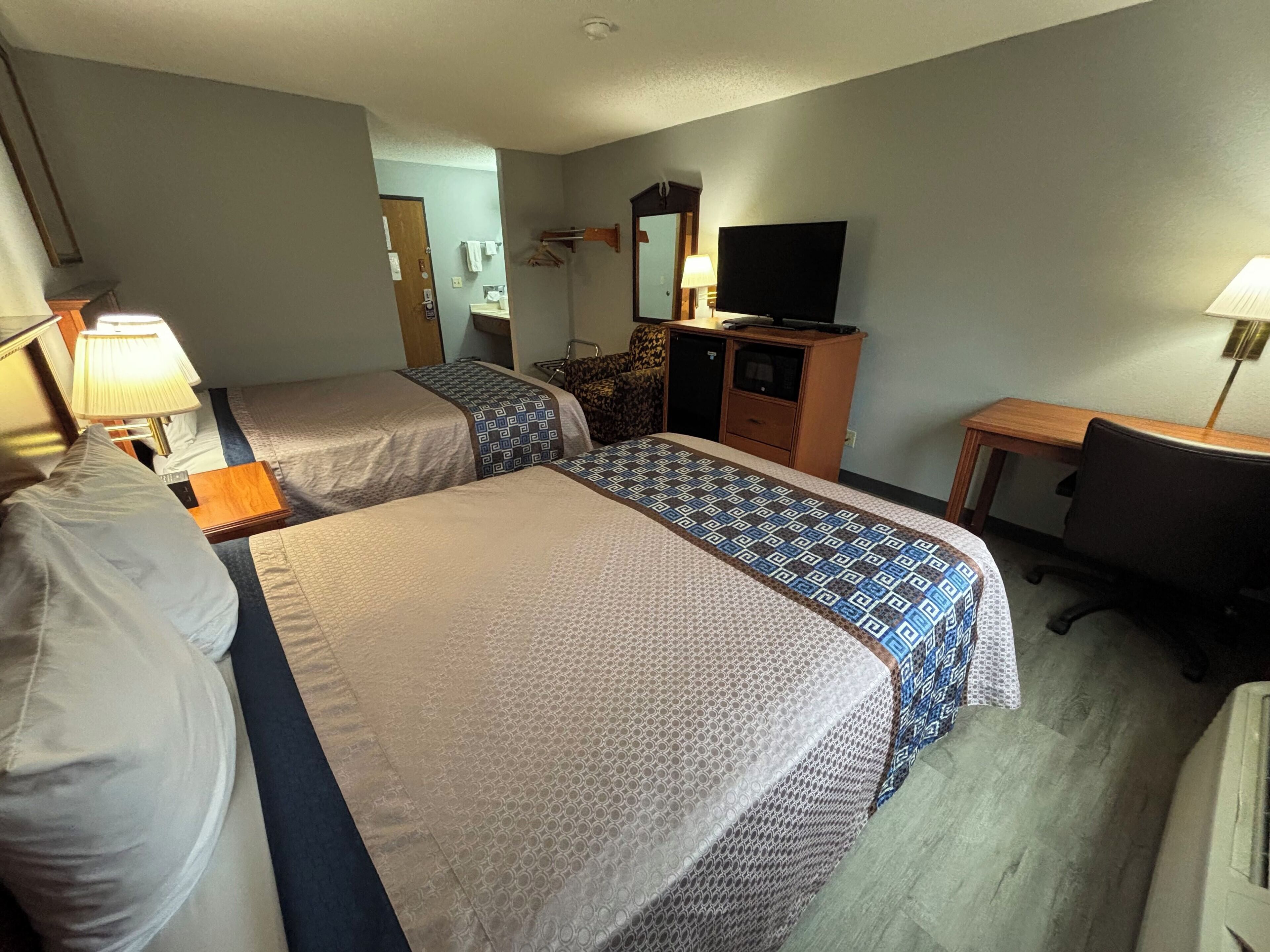 Une chambre d’hôtel avec deux lits, un bureau, une chaise, une télévision et une salle de bain visible au fond.