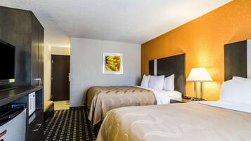 A hotel room with two beds, a TV, a desk, and a lamp.
