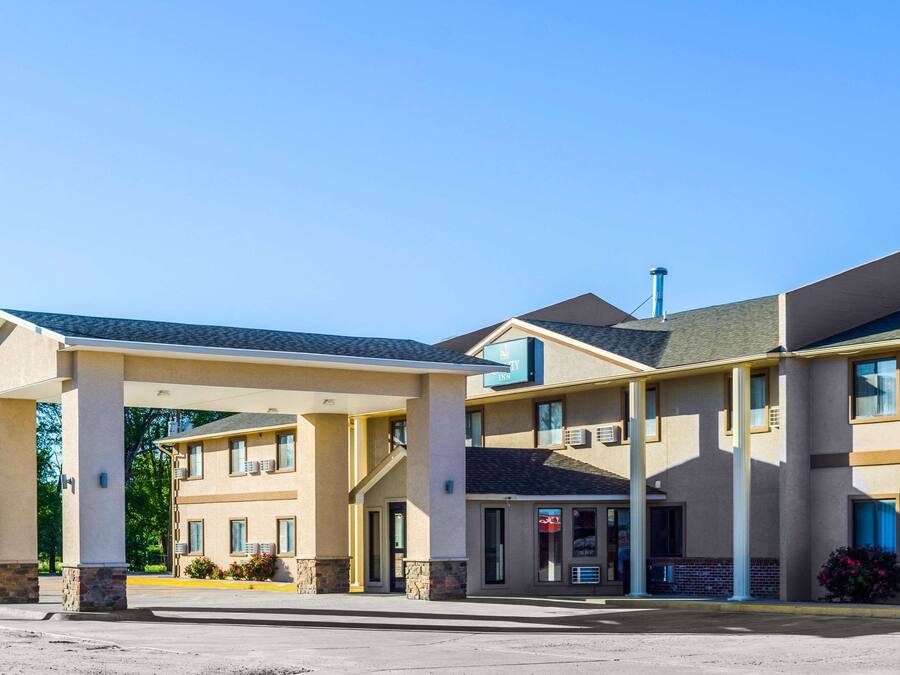 Un motel de dos pisos con estacionamiento cubierto, varias ventanas y un letrero visible.