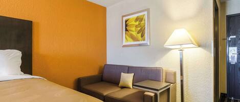 A hotel room with a bed, a sofa, a small table, a lamp, and a framed picture on the wall.