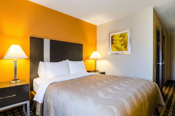 Habitación de hotel con cama, dos lámparas de noche, mesita de noche, un cuadro en la pared y una puerta con diseño a rayas.