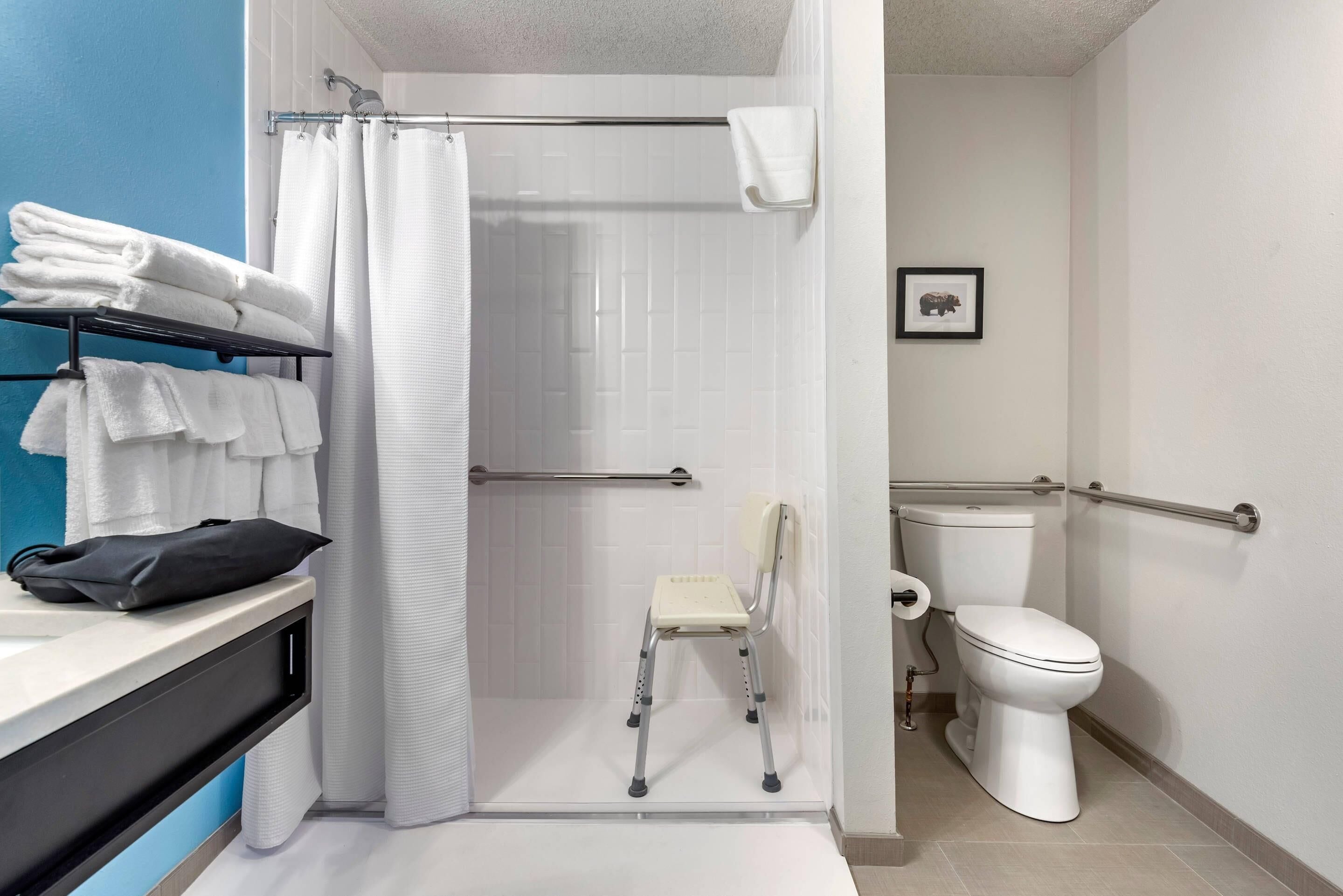 Un baño con ducha, inodoro, silla y toallero.