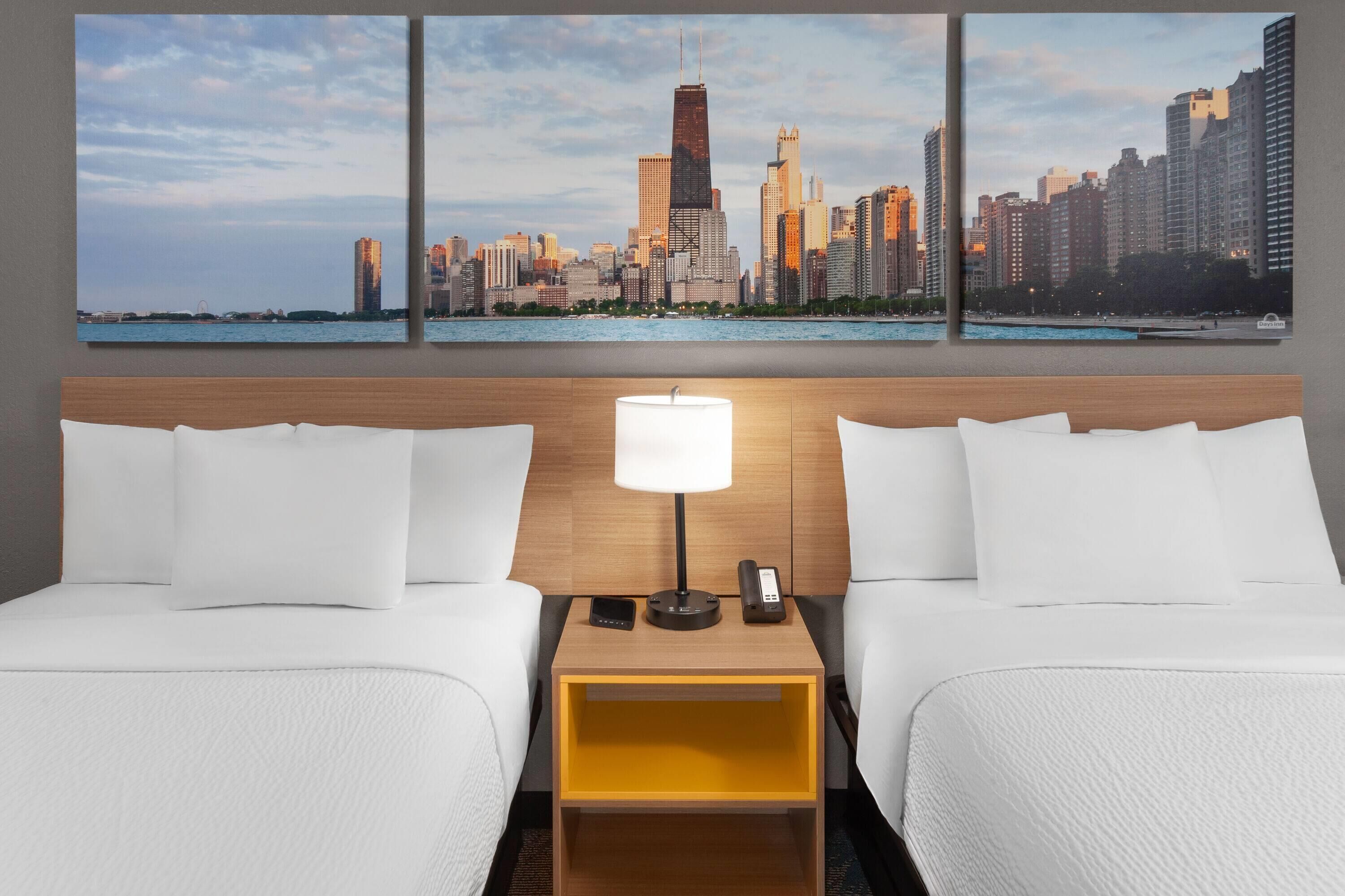 A hotel room with two beds, a nightstand with a lamp, a phone, and a cityscape view.