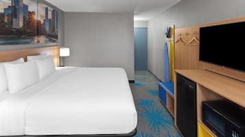 A hotel room with a large bed, a flat-screen TV, a minibar, and a cityscape painting on the wall.