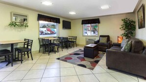 A living room with a sofa, chairs, a coffee table, a TV, and a window with a view of parked cars. - Super 8 by Wyndham Lewiston (Lewiston)