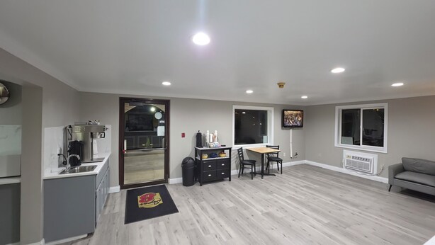 A modern kitchen with a coffee machine, a dining area with a table and chairs, a TV mounted on the wall, and a grey sofa. - Super 8 by Wyndham Lewiston (Lewiston)