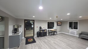 A modern kitchen with a coffee machine, a dining area with a table and chairs, a TV mounted on the wall, and a grey sofa. - Super 8 by Wyndham Lewiston (Lewiston)