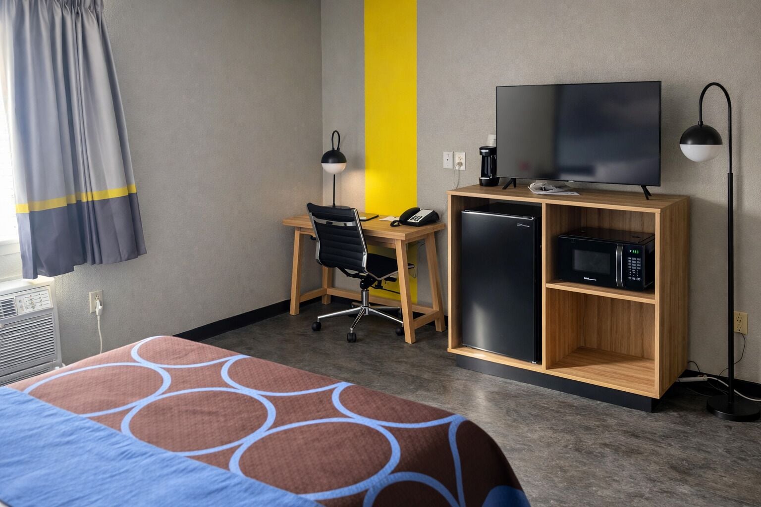 A hotel room with a bed, a desk with a chair, a television, a microwave, and a coffee maker.
