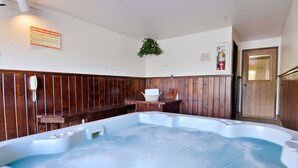 Un jacuzzi dans une pièce aux murs recouverts de lambris en bois, un panneau d’avertissement, un extincteur et une porte.