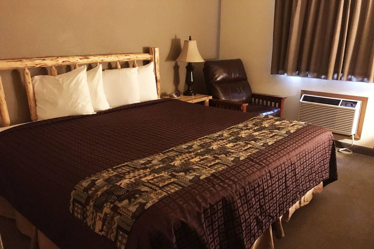 A hotel room with a large bed, a chair, a lamp, and an air conditioning unit.