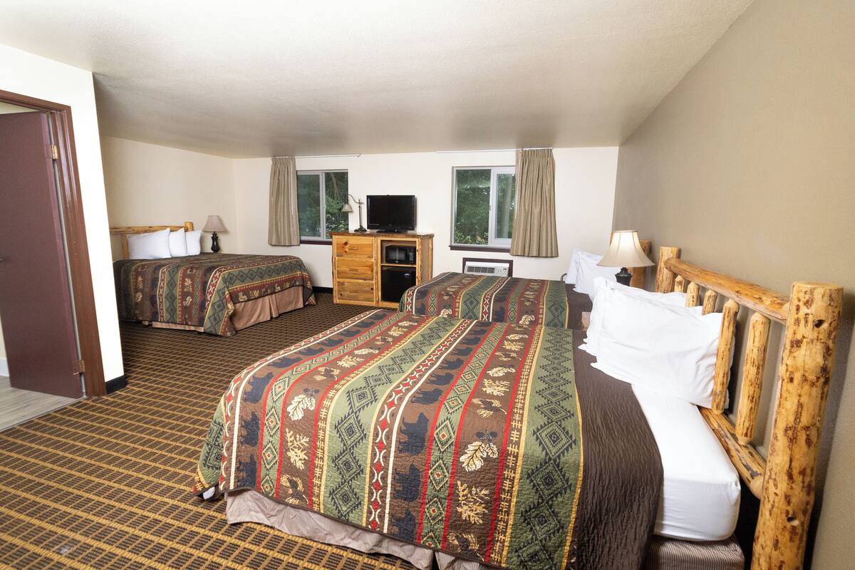 A hotel room with two beds, a wooden headboard, a television, and a dresser.