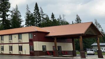 A two-story building with a red roof and beige walls, featuring a covered entrance area with benches.