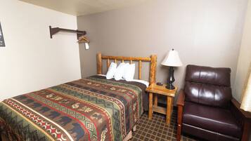 A hotel room with a large bed, a wooden nightstand, a leather armchair, and a wall-mounted coat rack.