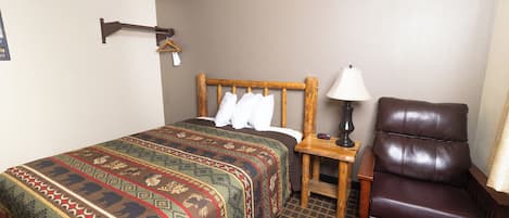 Een hotelkamer met een groot bed, een houten nachtkastje, een leren fauteuil en een wandkapstok.