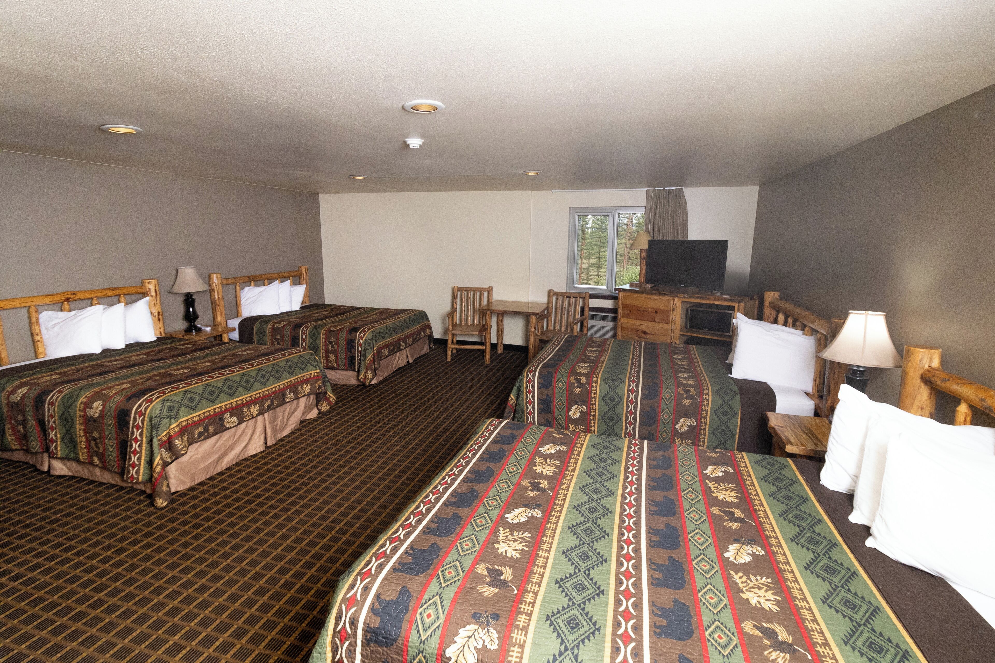 A hotel room with two beds, a desk, a television, and a window.
