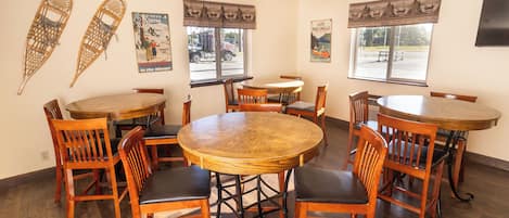 A dining area with wooden tables and chairs, two posters on the walls, and large windows with curtains.