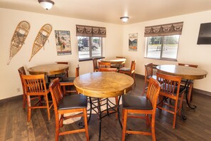 A dining area with wooden tables and chairs, two posters on the walls, and large windows with curtains.