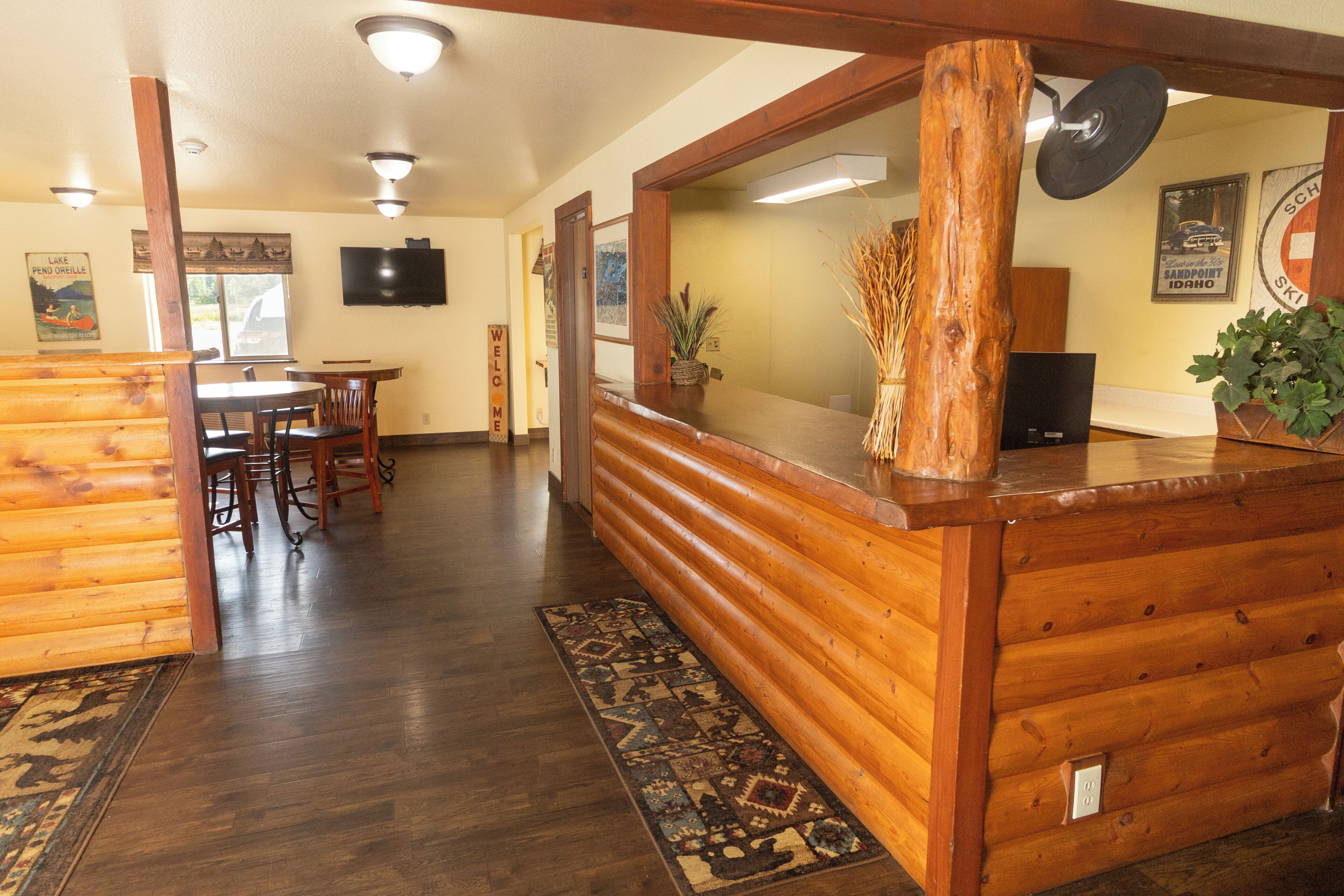A wooden reception desk with a flat-screen TV, a 'Welcome' sign, and a ski-themed poster on the wall.