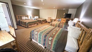 Une chambre d’hôtel avec deux lits, un bureau, une chaise, une télévision et une salle de bain visible à travers une porte ouverte.