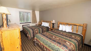 A room with two beds, a wooden dresser, a window with a view of trees, and a patterned carpet.