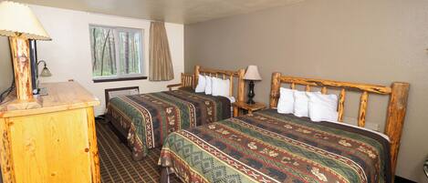 A room with two beds, a wooden dresser, a window with a view of trees, and a patterned carpet.