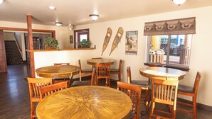 Un espace repas avec des tables et des chaises en bois, un escalier et une fenêtre donnant sur les voitures garées.