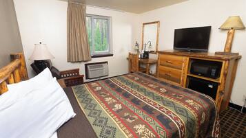 Habitación de hotel con cama, televisión, escritorio con computadora, espejo y ventana con cortinas.