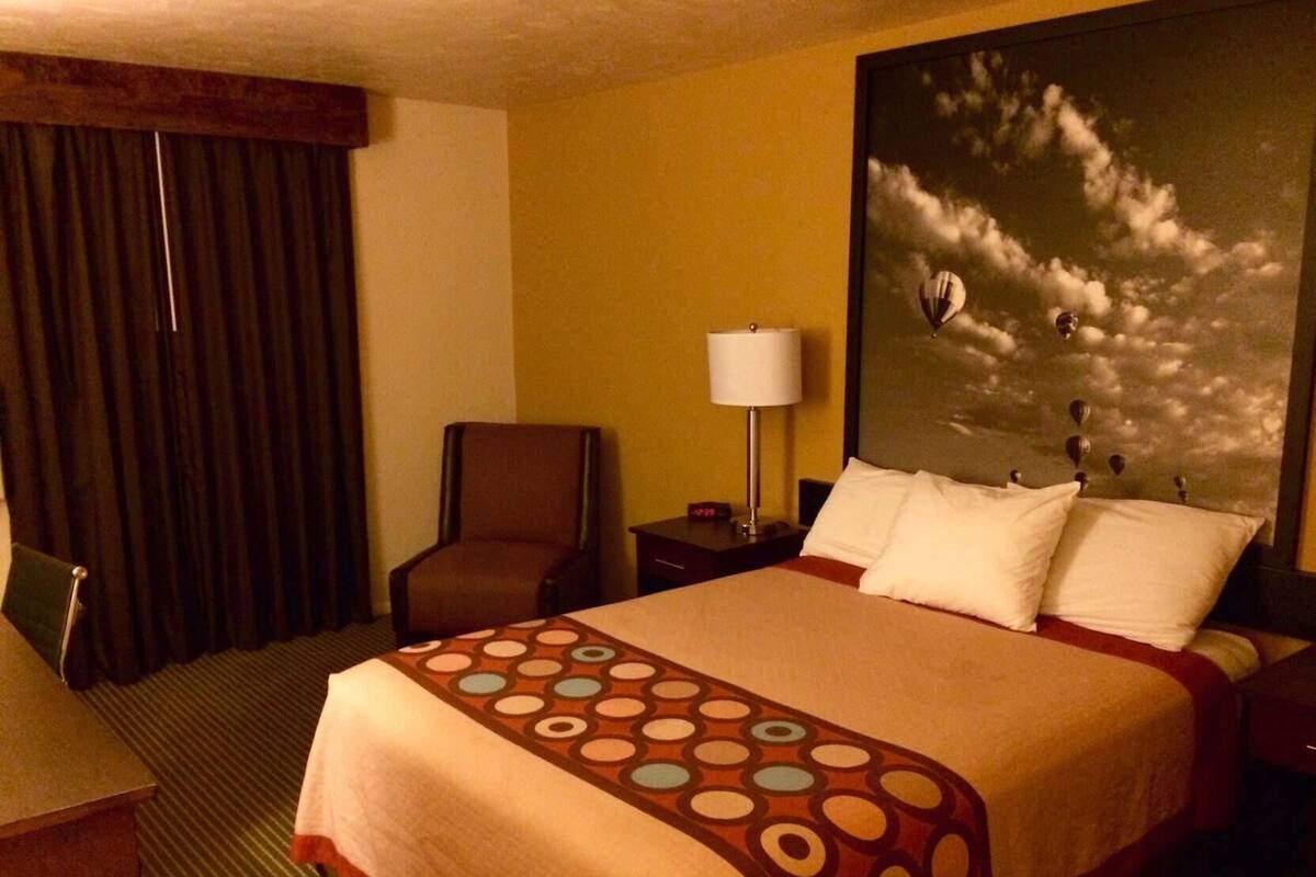 Une chambre d’hôtel avec un lit, une chaise, une lampe et un tableau représentant des nuages.