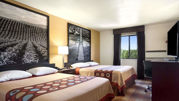 A hotel room with two beds, a desk, a TV, and a large window.