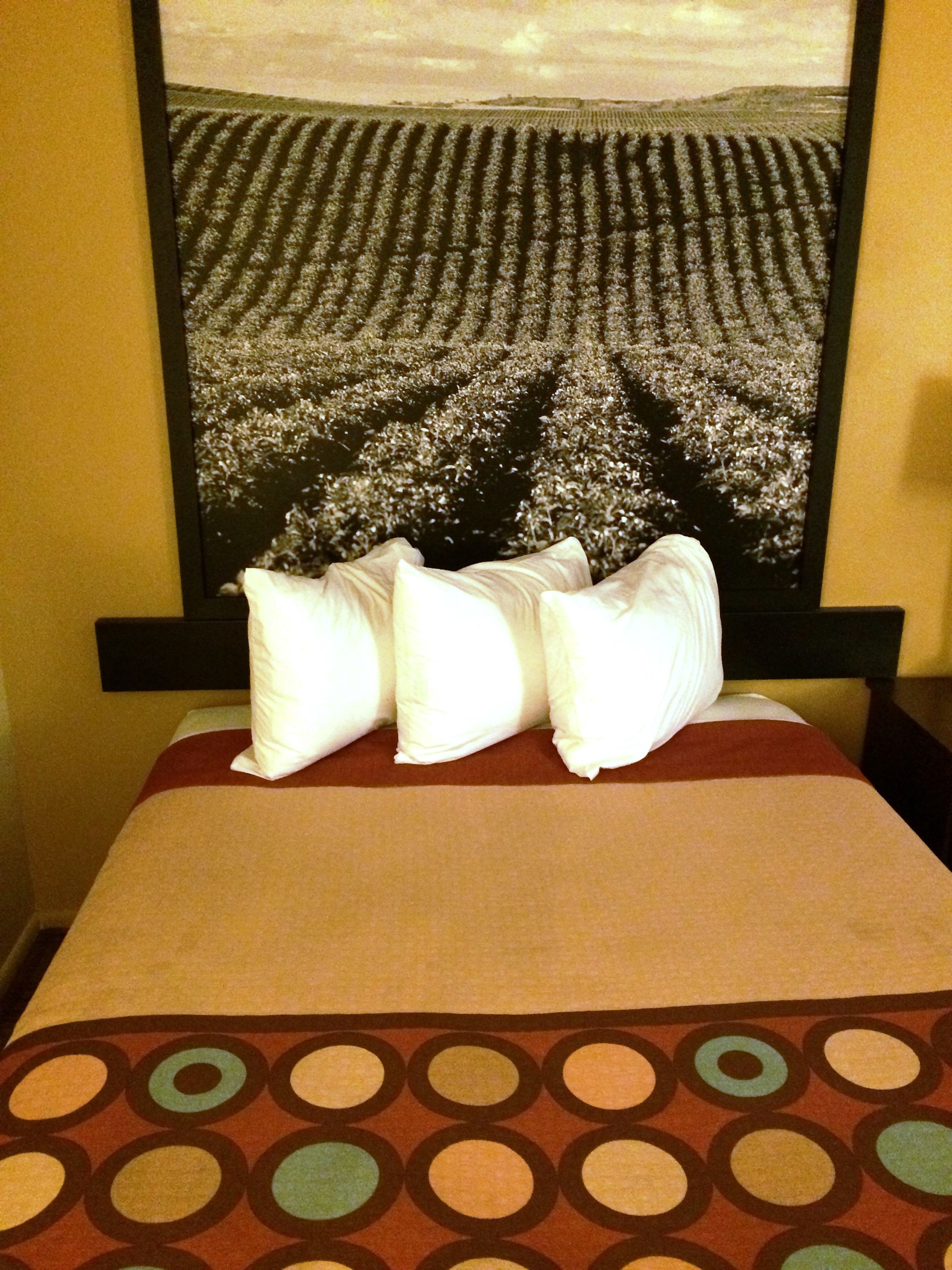 A hotel room with a bed, pillows, and a large framed picture on the wall.