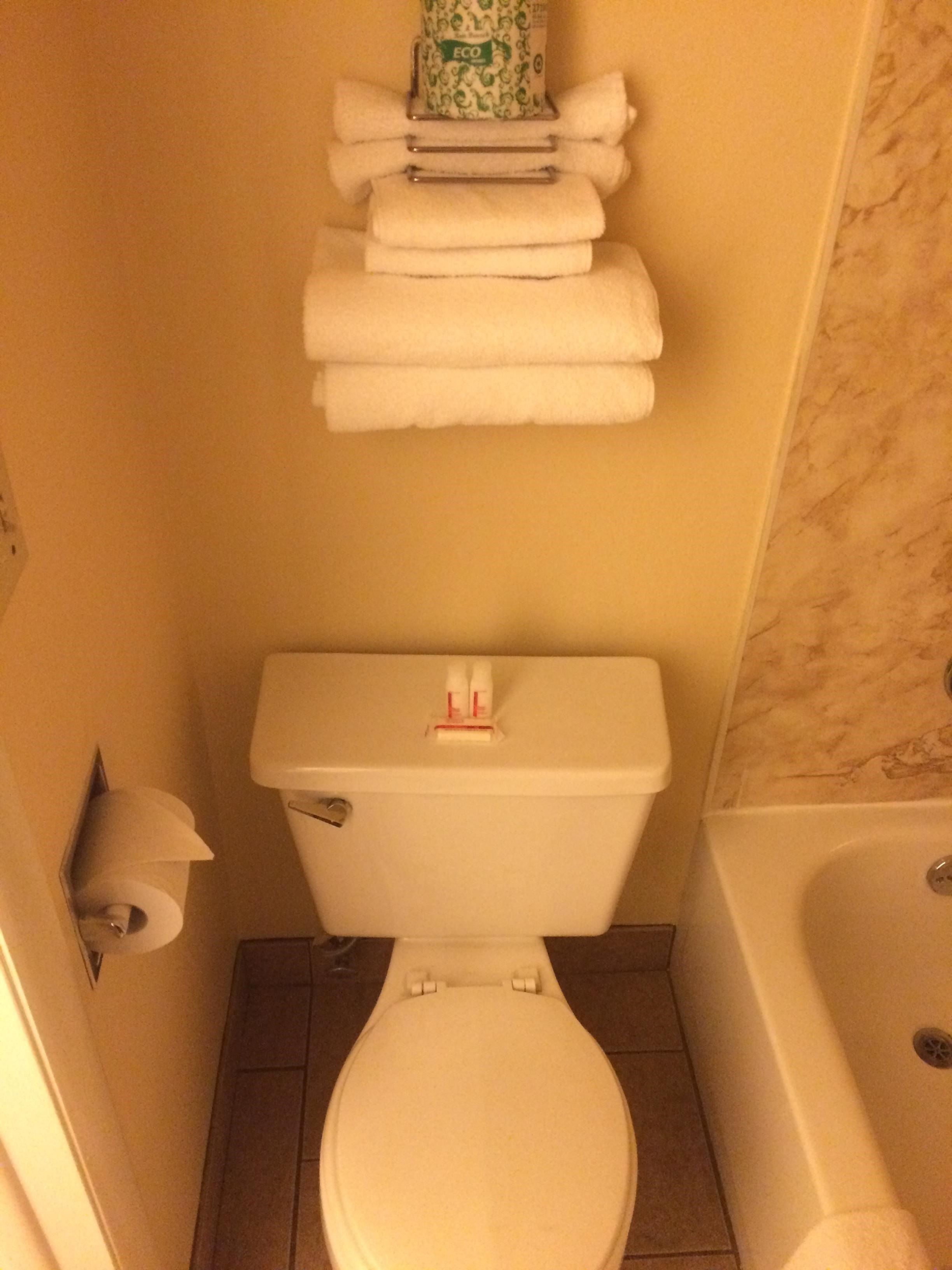 A bathroom with a toilet, a stack of white towels, and a roll of toilet paper on the wall.