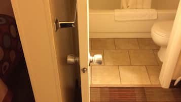 A bathroom with a toilet, a shower, and a door leading to another room.