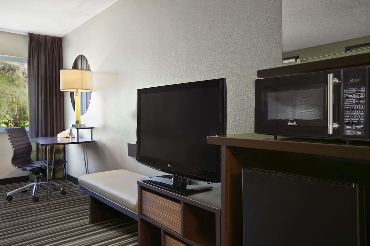 Hotelkamer met flatscreen-tv, magnetron, bureau met lamp, stoel en bed.
