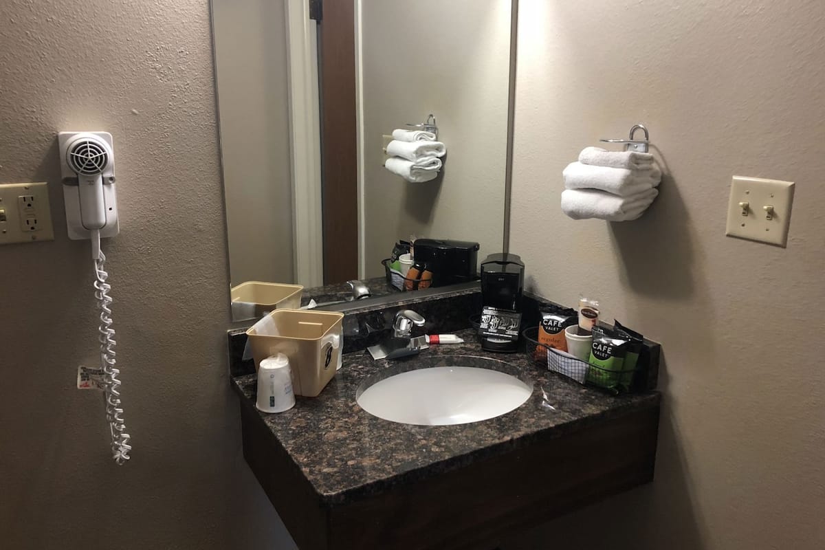 Een hotelbadkamer met een wastafel, spiegel, handdoekhouder en een haardroger aan de muur.