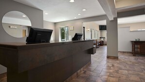 A reception area with a dark reception desk, a round mirror, and a view into a dining area with chairs and tables.