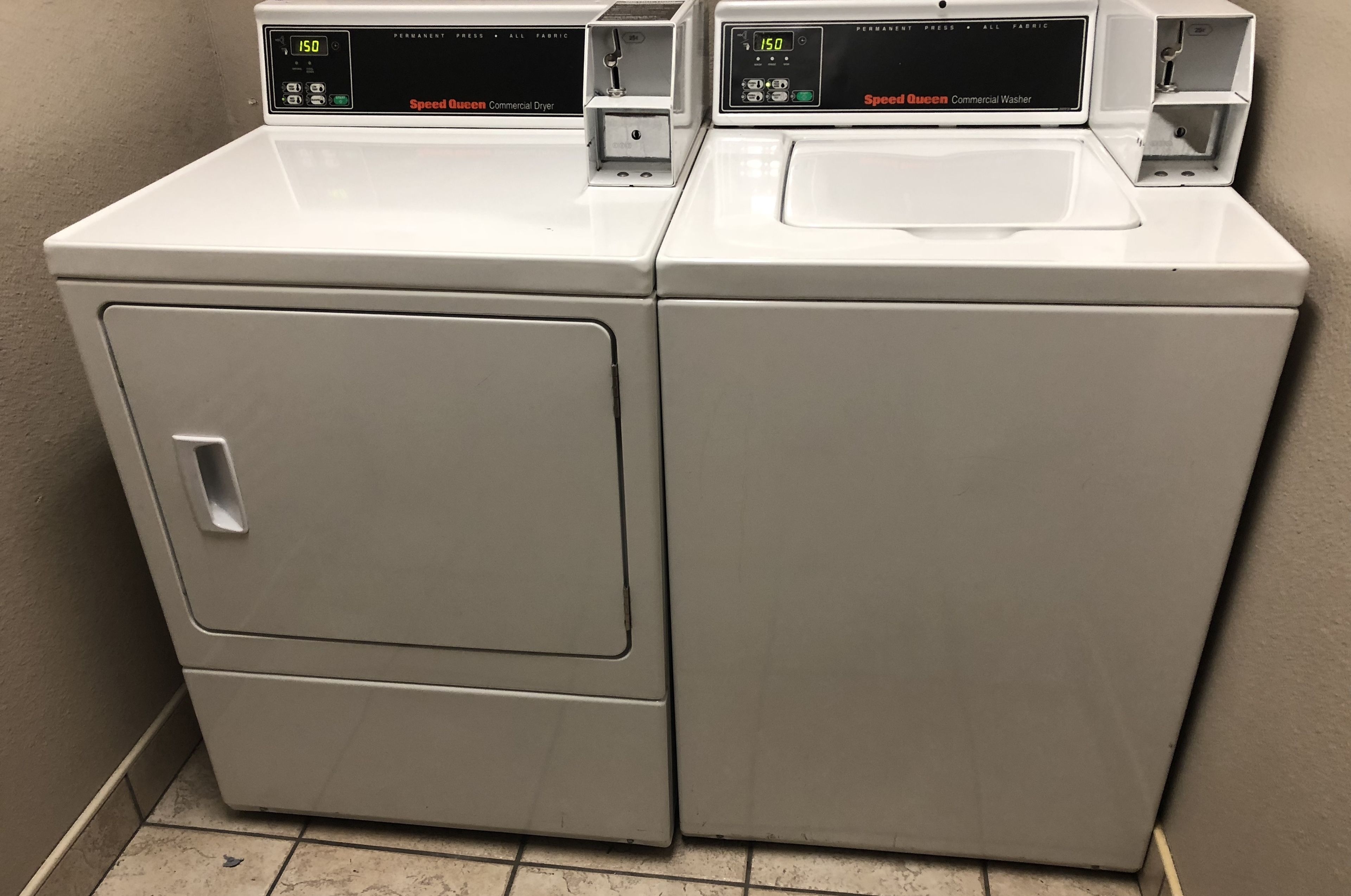 Two white commercial washers with digital displays, one labeled "Speed Queen Commercial Dryer" and the other "Speed Queen Commercial Washer."