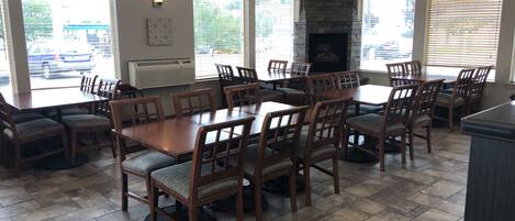 Un vaste espace dédié à la salle à manger, avec une grande table en bois entourée de chaises, une cheminée en pierre et de grandes fenêtres offrant une vue sur l’extérieur.
