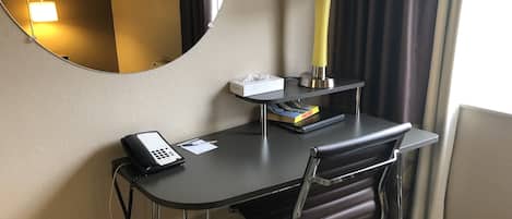 Ein Hotelzimmer mit Schreibtisch, Stuhl, Lampe und Spiegel.