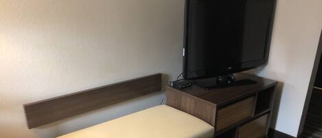 Habitación de hotel con una cama individual, un televisor de pantalla plana montado en un mueble de madera y un escritorio pequeño con cajones.